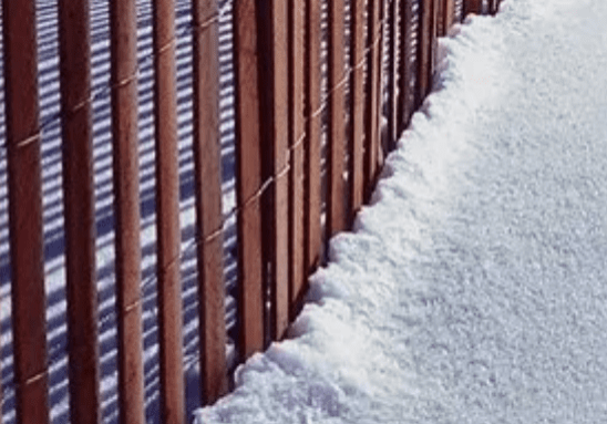 Wooden fence beside snowy ground.