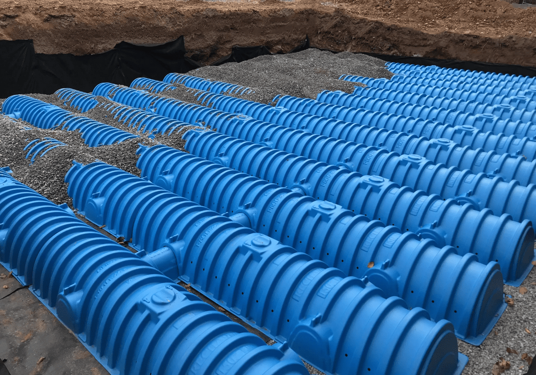 Blue plastic drainage pipes in gravel.